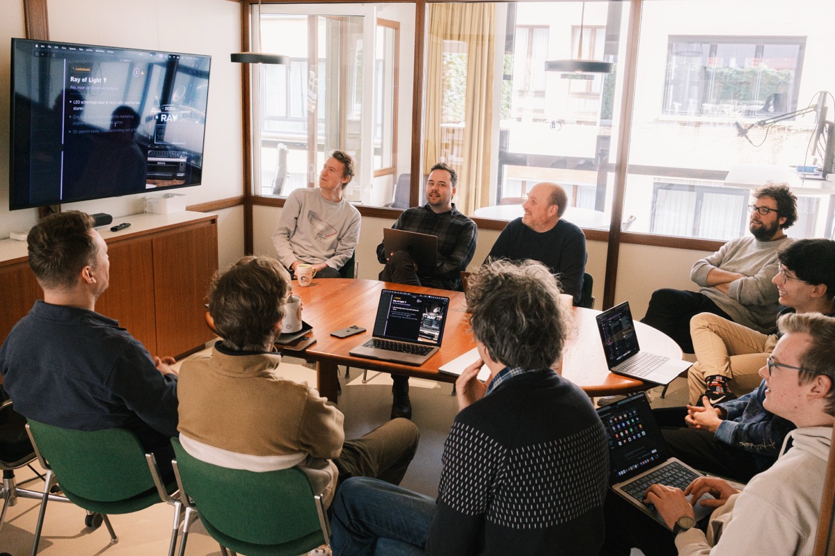 The Spatie team sitting around a table in the Antwerp office, laptops open, watching a presentation on the wall screen.